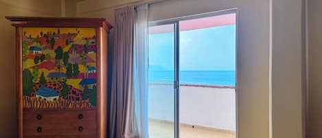 A room with a large wooden dresser, a sliding glass door leading to a balcony with a view of the sea.