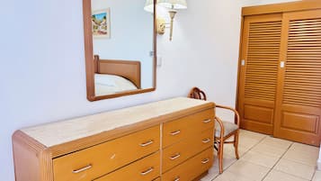A bedroom with a wooden dresser, a chair, a bed, a mirror, and a wall-mounted lamp.