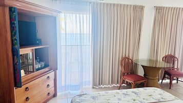 Een hotelkamer met een bed, een houten kledingkast, een glazen tafel met stoelen en uitzicht door de gordijnen.