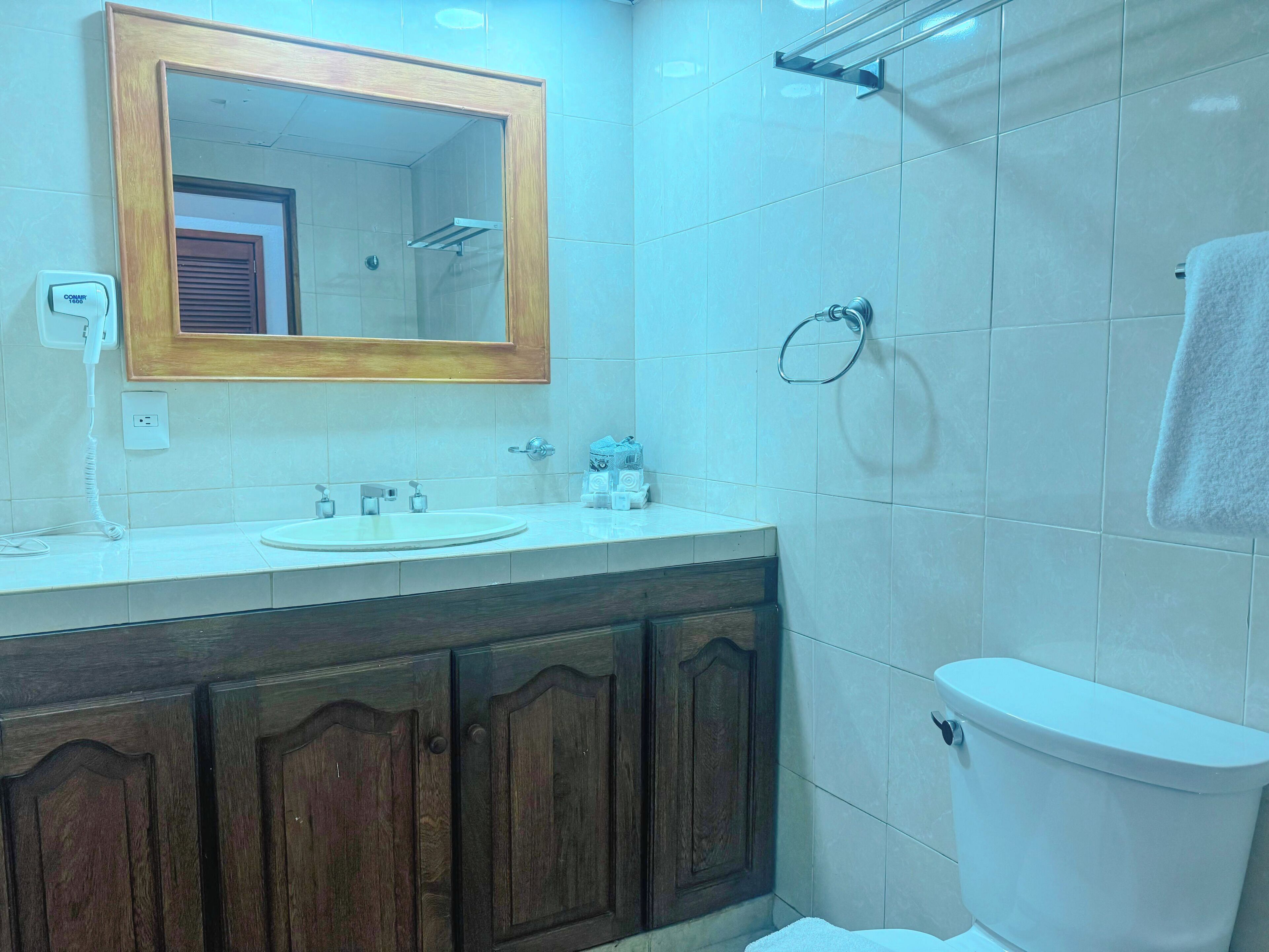 A bathroom with a wooden vanity, a white sink, a mirror, a toilet, and a towel rack.
