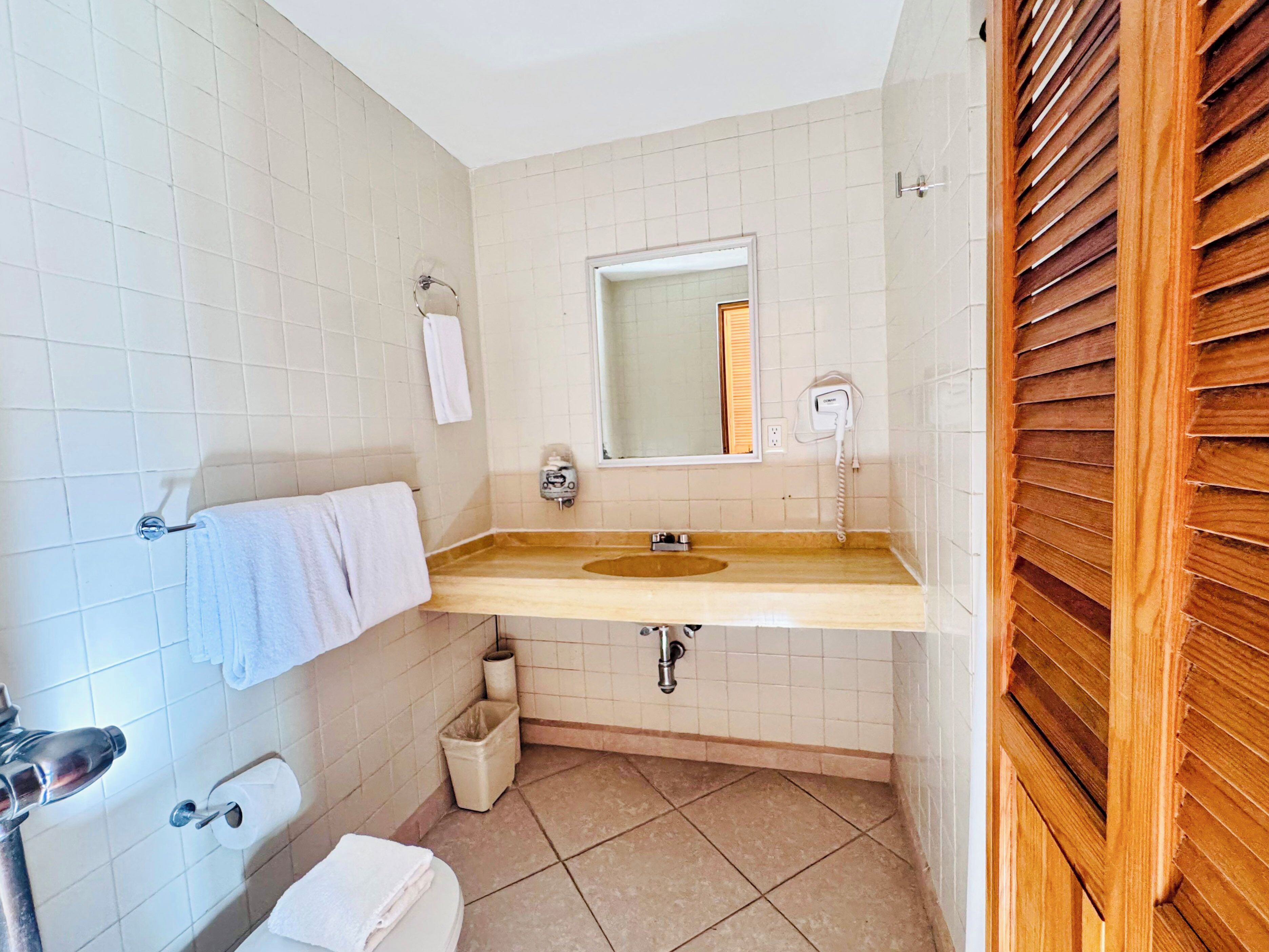 Un baño con lavamanos, espejo, toallero, inodoro y un cubo de basura.