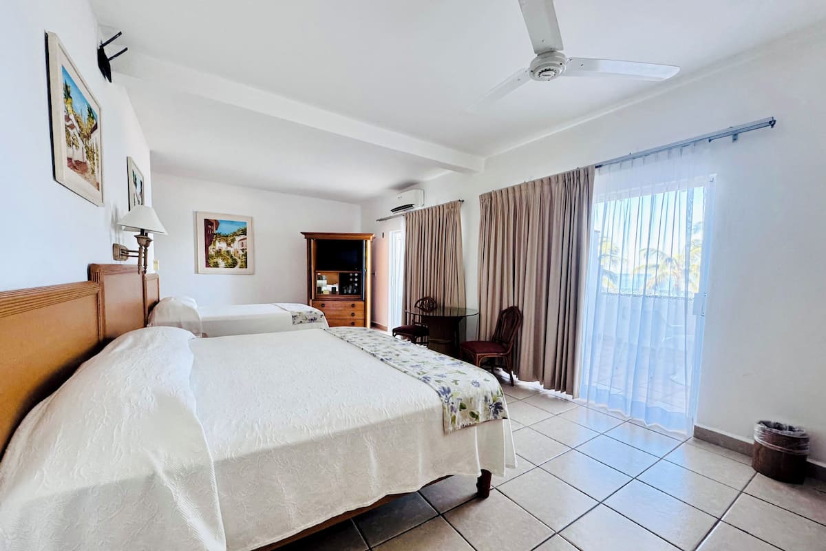 Habitación de hotel con cama, escritorio, silla, ventilador de techo y vistas al exterior.