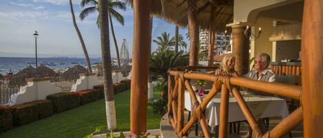 Un restaurant offrant une vue sur la plage et l’océan, doté d’un toit de chaume et de balustrades en bambou.