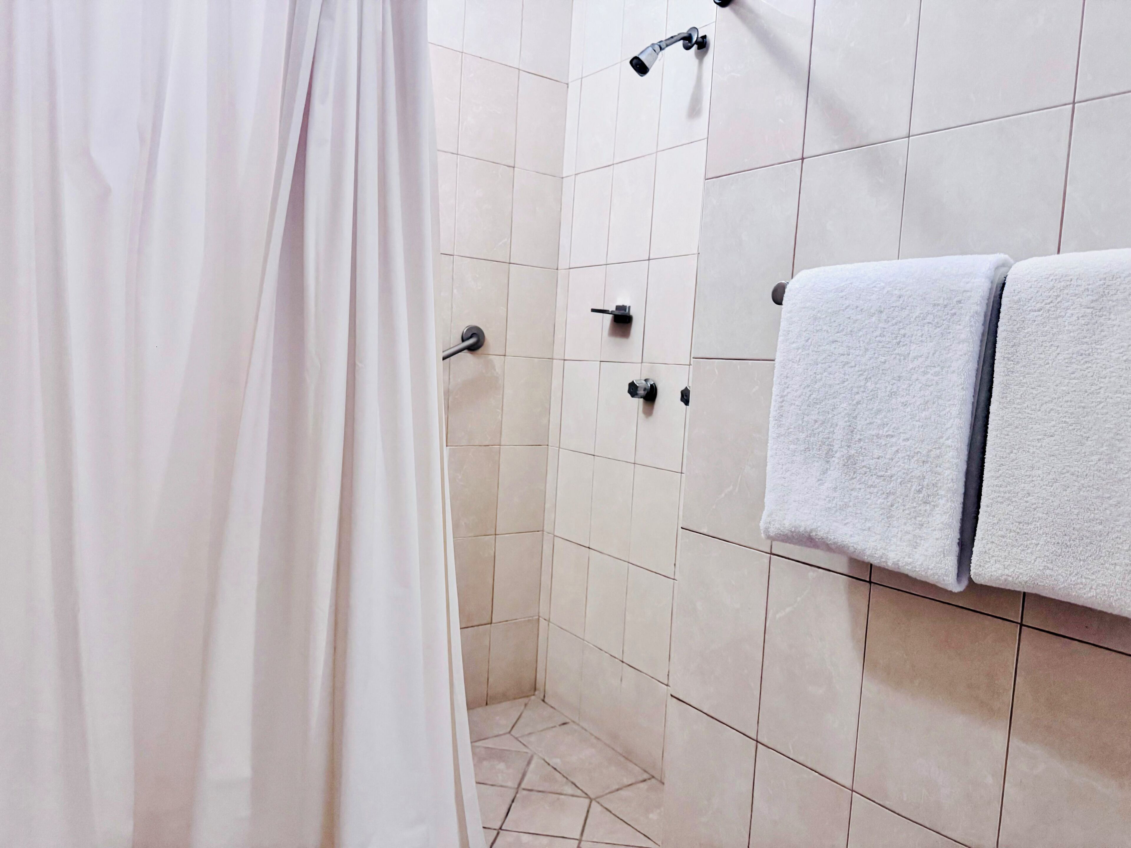 A bathroom with a shower curtain, tiled walls, a towel rack with towels, and a handheld showerhead.