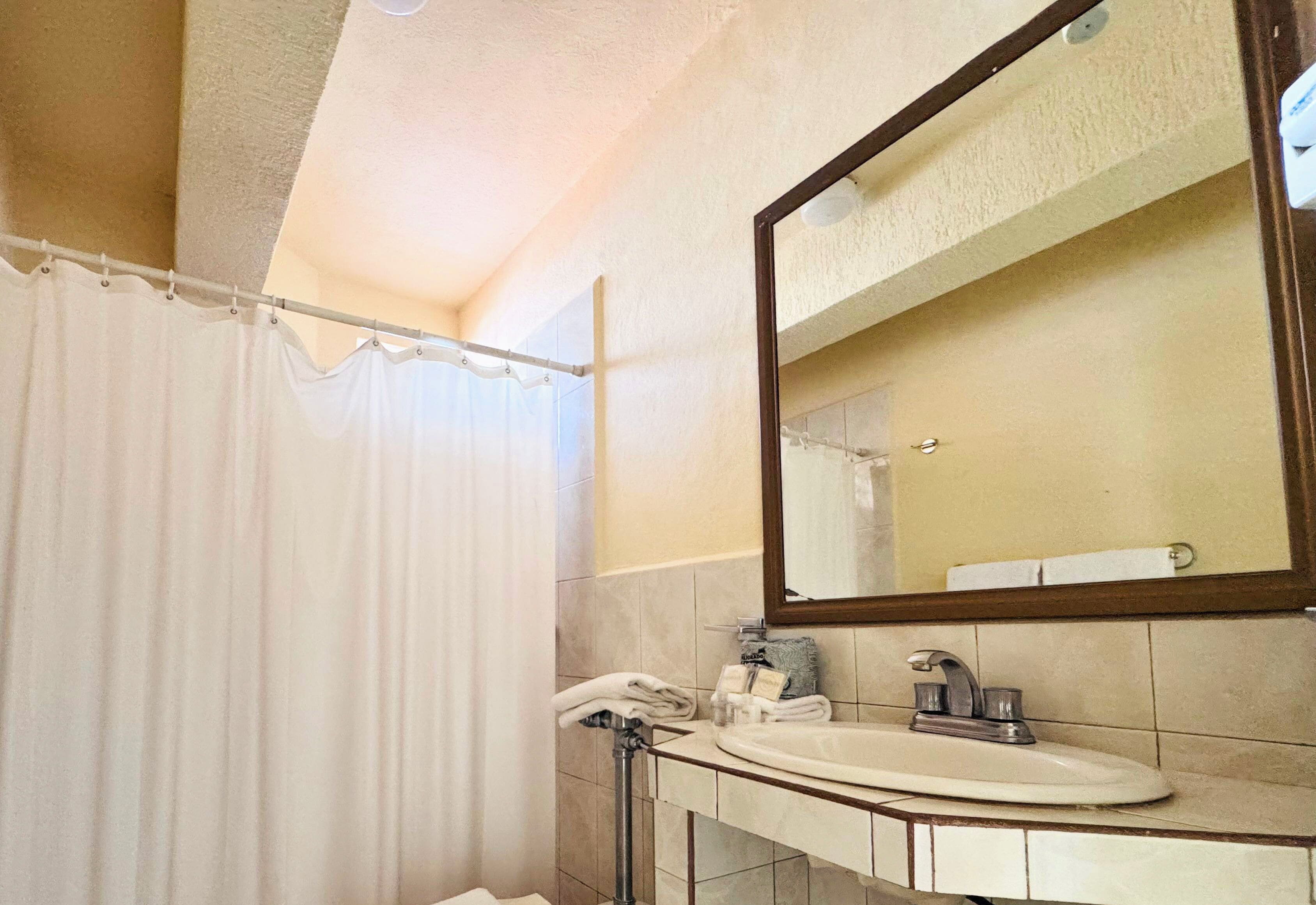 A bathroom with a shower curtain, a sink, a mirror, and a towel rack.