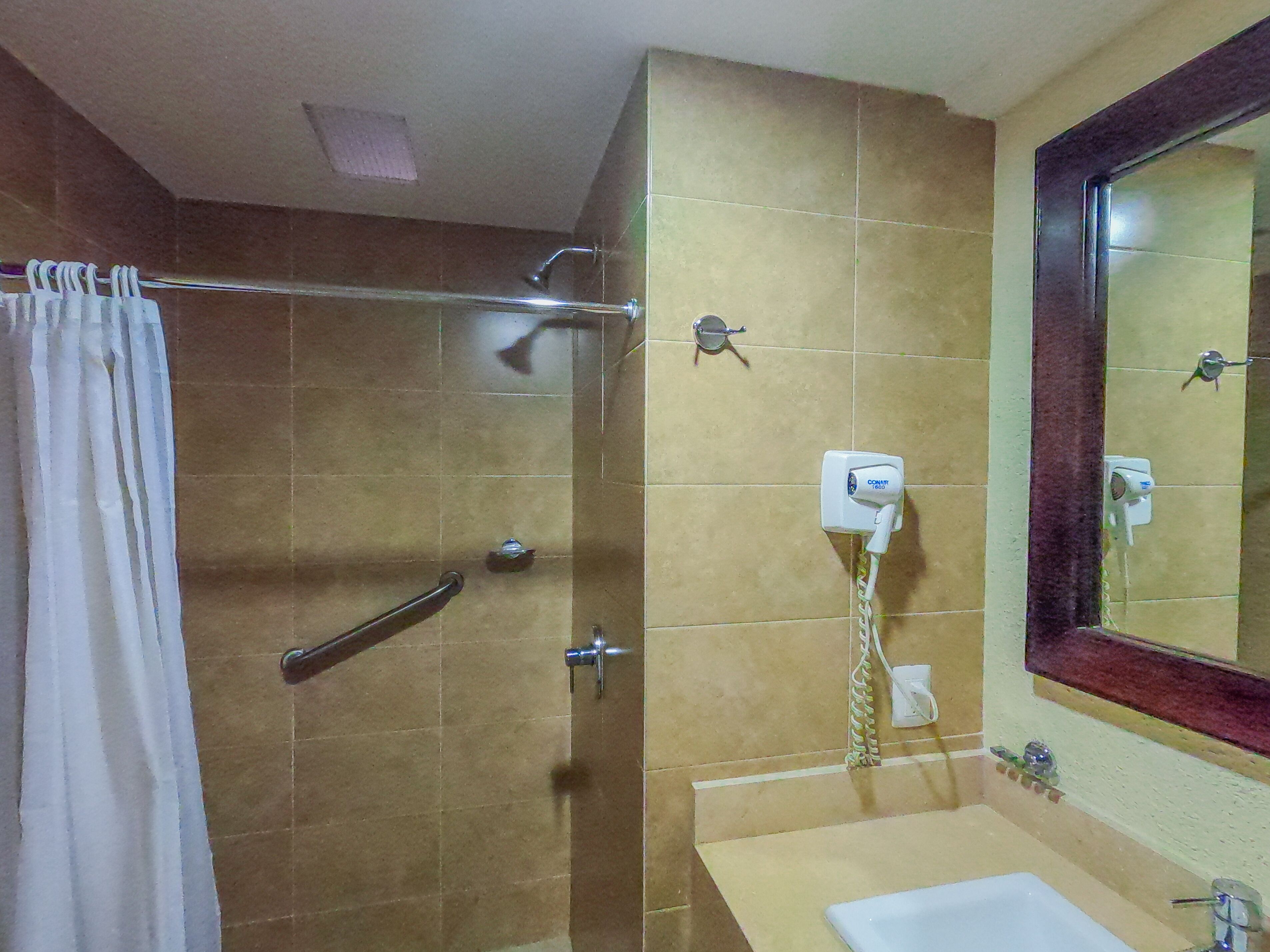 A bathroom with a shower, a handrail, a towel rack, a sink, and a mirror.