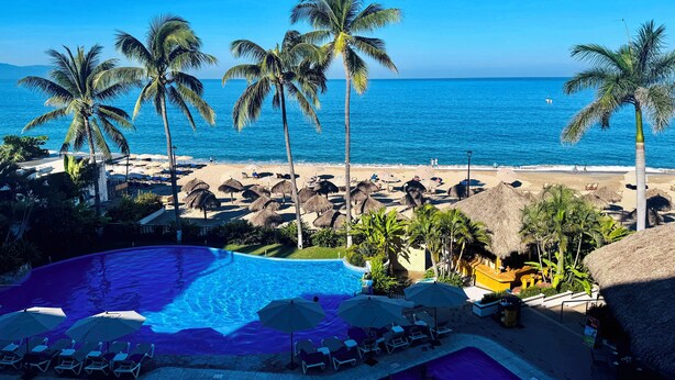 Een resort met een zwembad, strand en palmbomen.