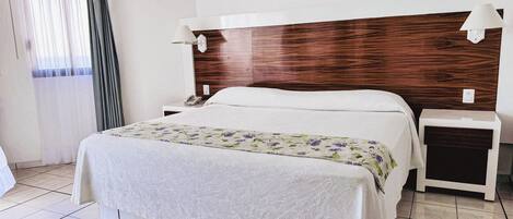 Ein Hotelzimmer mit Bett, Nachttischen, einem Telefon und einem Fenster mit Vorhängen.