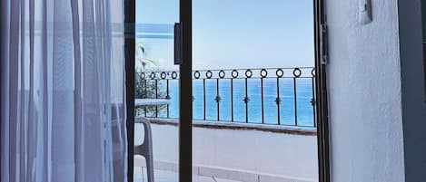 A room with a sliding glass door leading to a balcony with a view of the sea.