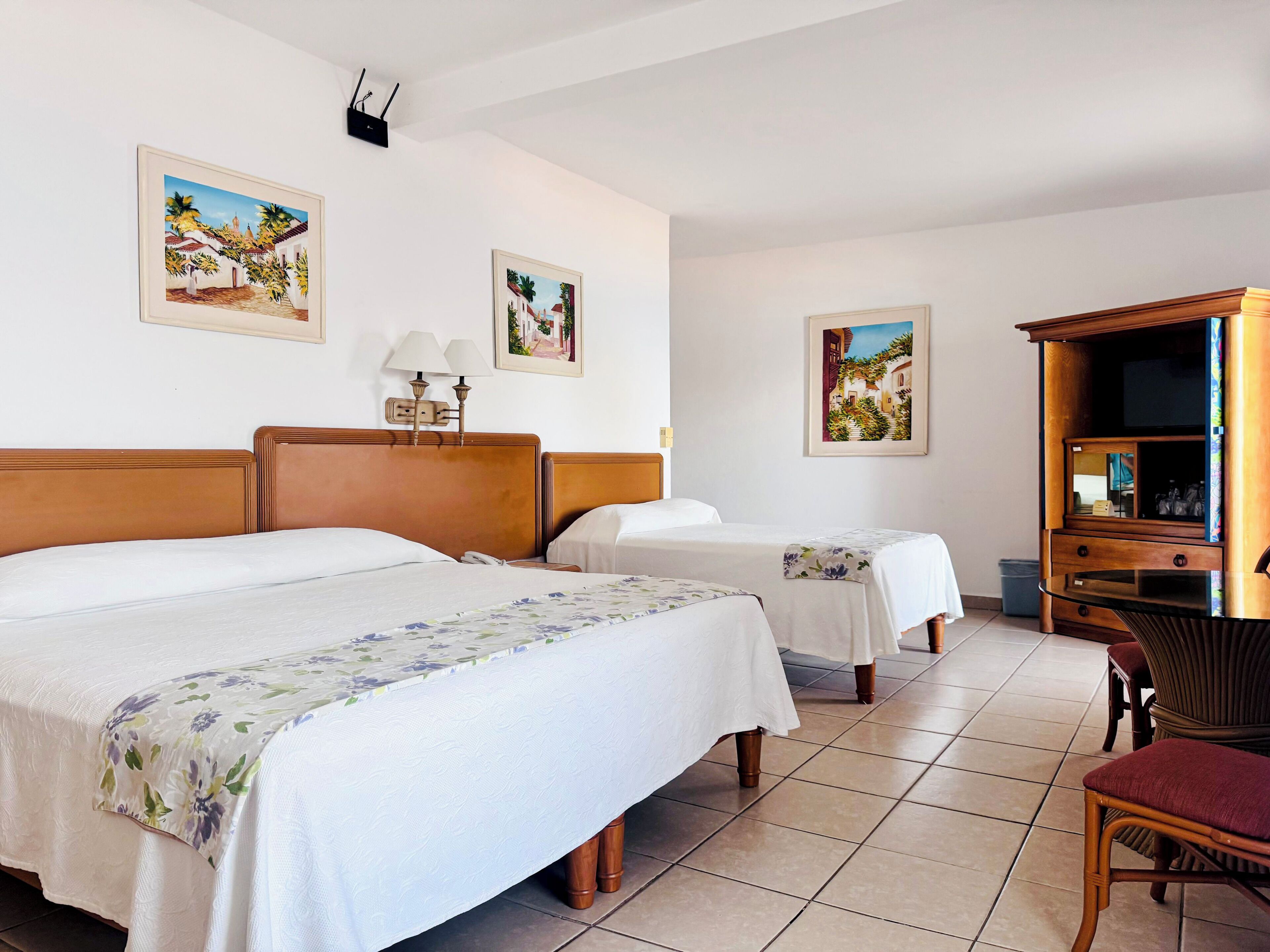 A hotel room with two beds, a wooden headboard, a TV cabinet, and artwork on the walls.