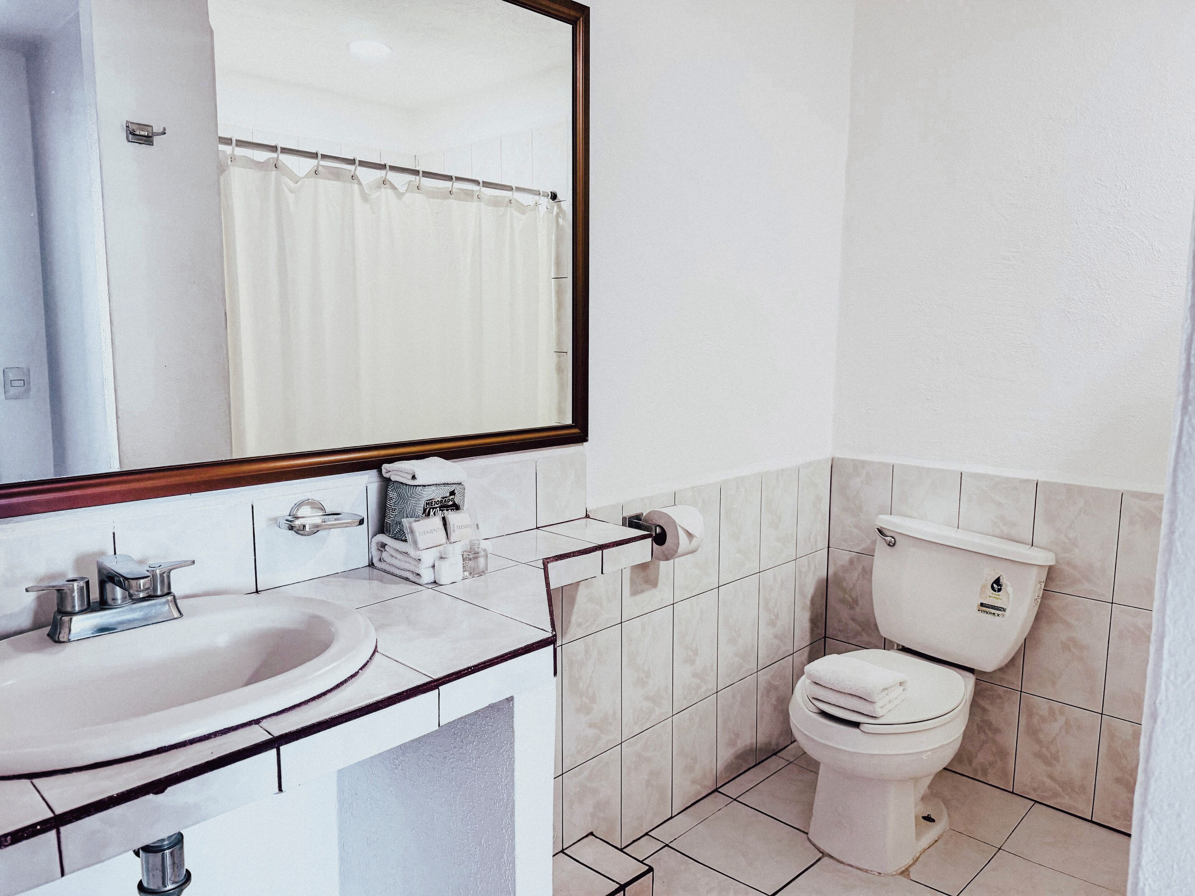 Un baño con lavamanos, espejo, inodoro y toallero.