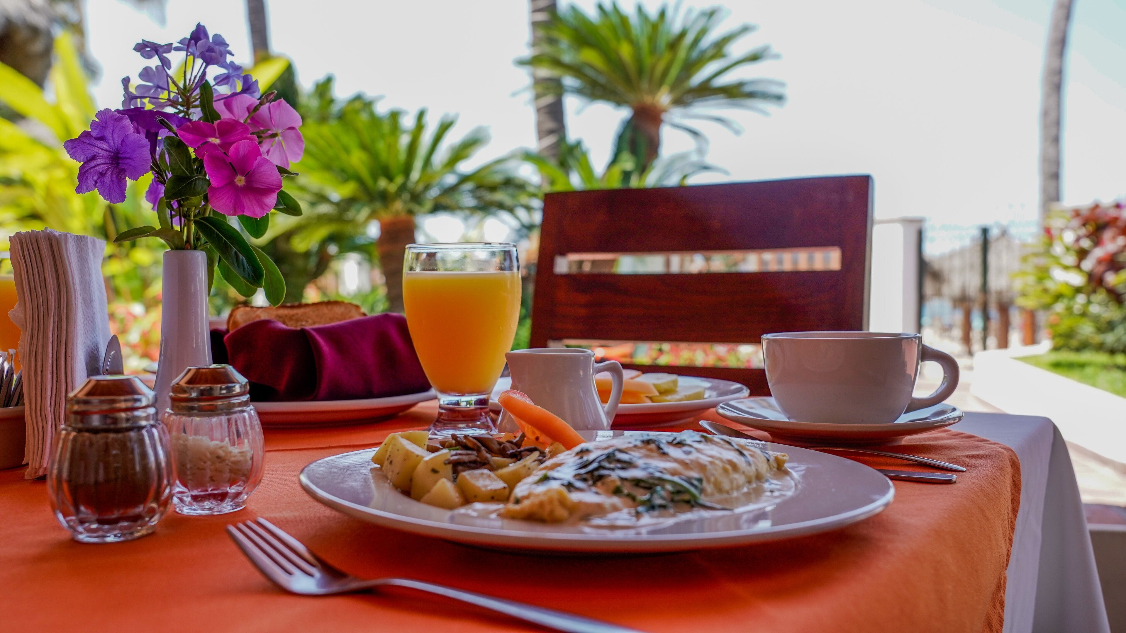 A breakfast table with plates of food, a glass of orange juice, and a cup.
