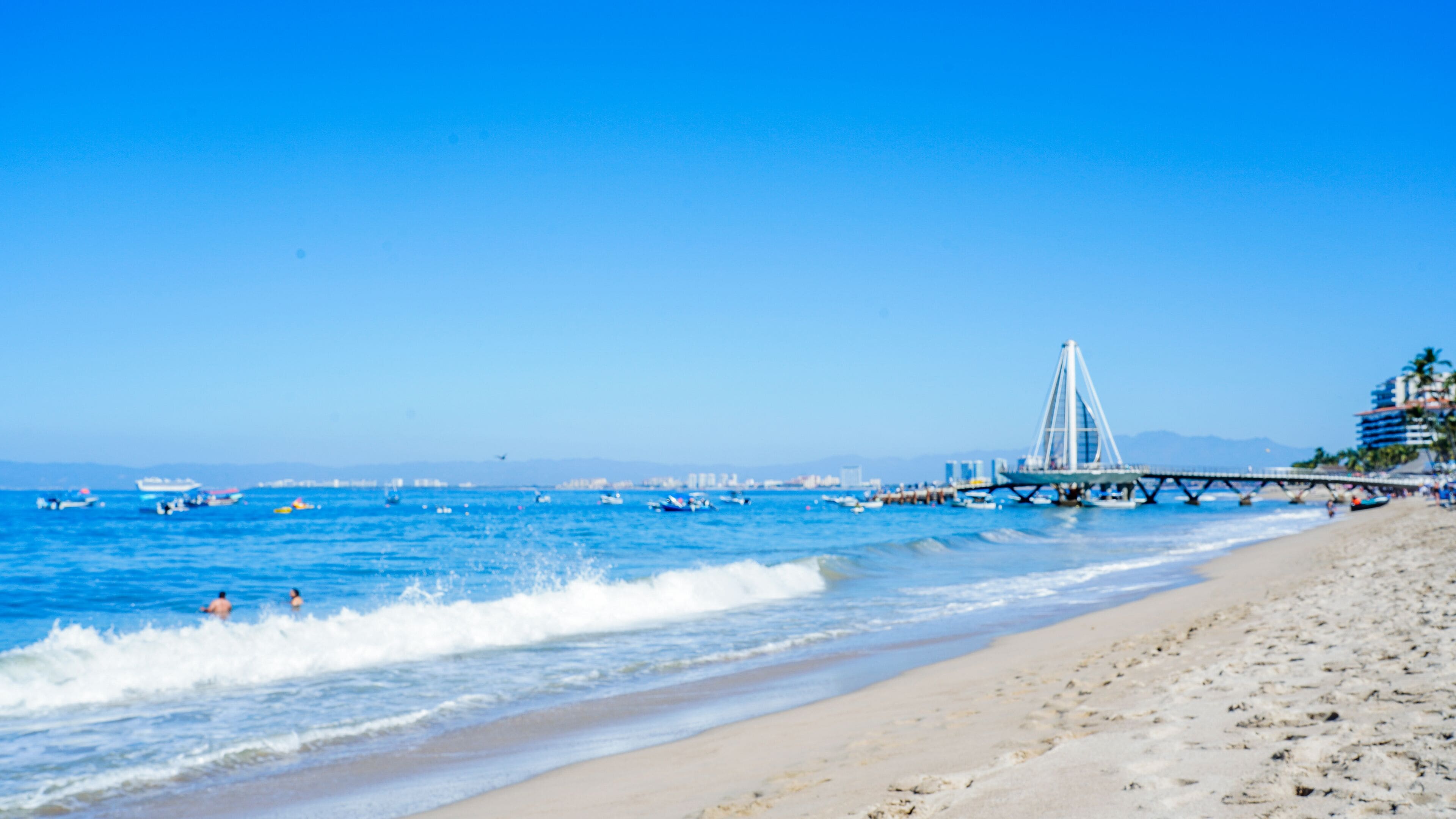 A beach with a bridge and boats in the water.