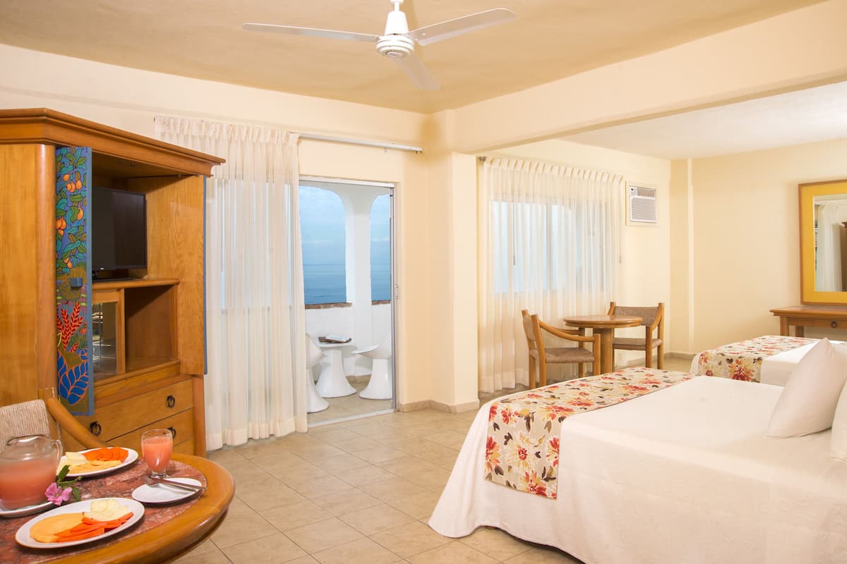 Habitación de hotel con cama, escritorio, silla, televisión y balcón con vista al mar.