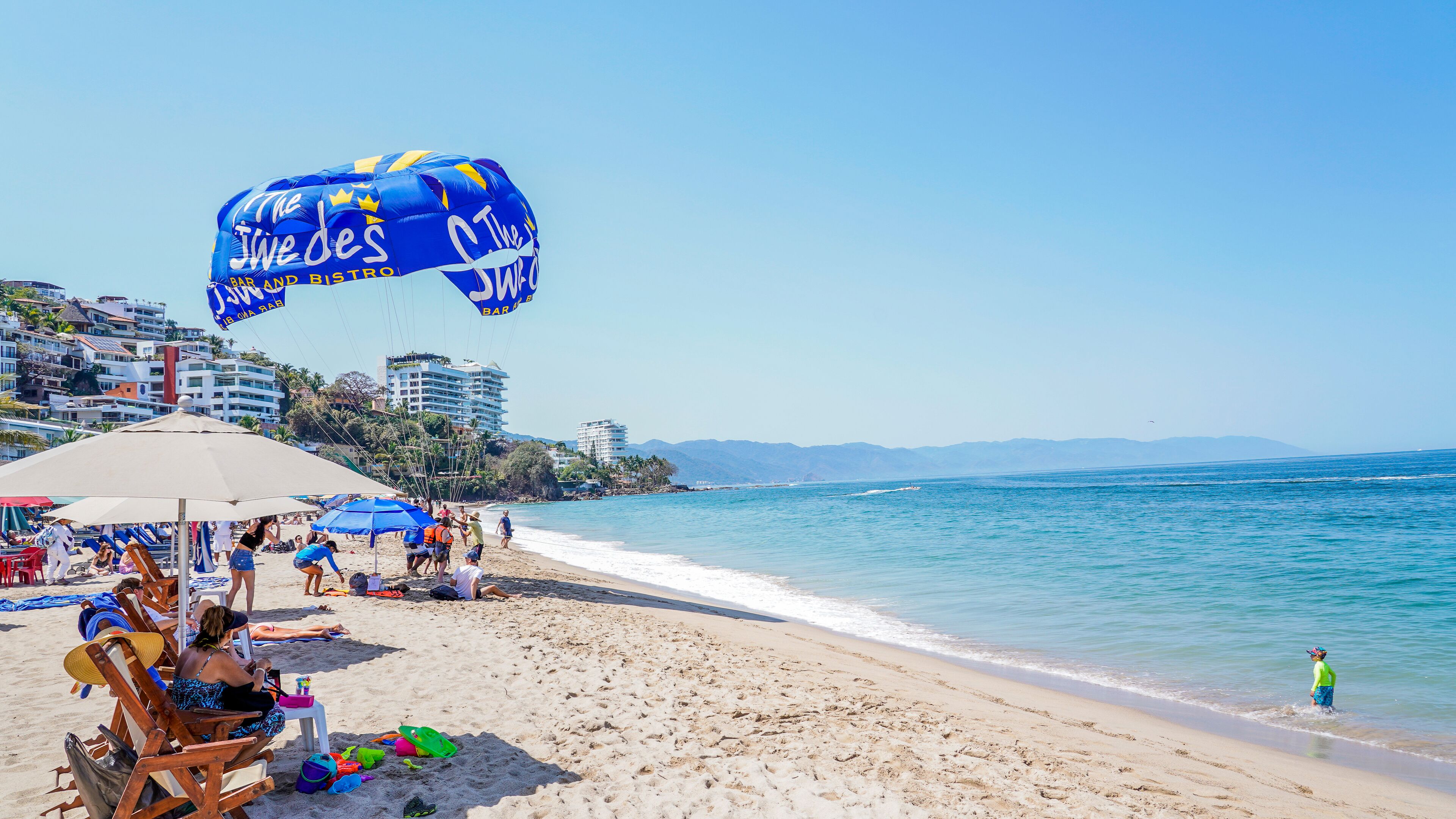 Una playa con sombrillas, sillas de playa y un paracaídas.