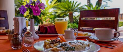 A breakfast setting with a plate of food, a glass of orange juice, a cup, and a vase with flowers.