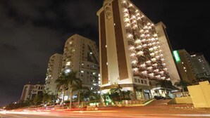 A high-rise building with multiple floors, illuminated windows, and a prominent vertical structure. - Plaza Rio Residences - Barra First (Rio de Janeiro)