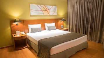 Une chambre d’hôtel avec un grand lit, deux tables de chevet, une lampe fixée au mur et une fenêtre avec des rideaux.