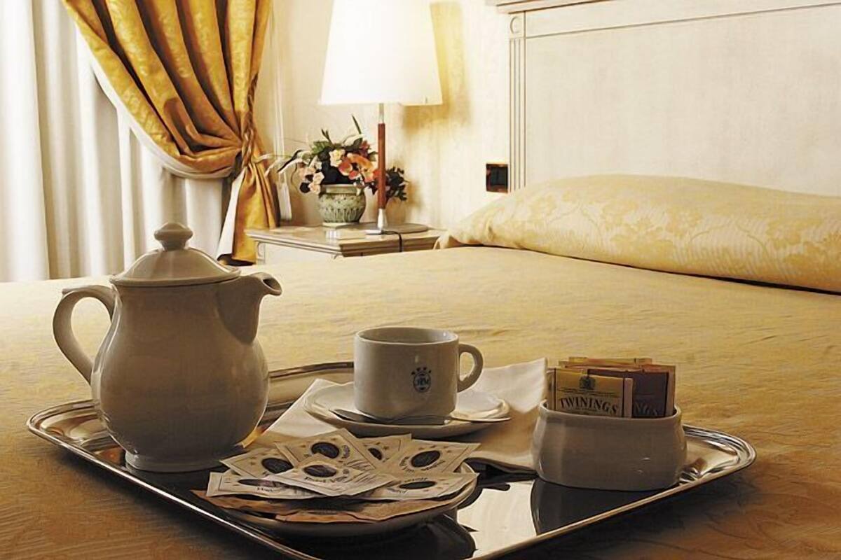 A neatly arranged breakfast tray with a teapot, a cup, and a small container of tea bags on a hotel bed.