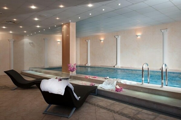A spa area with a pool, lounge chairs, and a small table with a vase of flowers. - Hotel Villa Medici (Rocca San Giovanni)