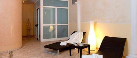 Un vestíbulo de hotel con una pared curva, una zona de estar con dos sillones, una mesita con una lámpara y un ventanal con paneles de vidrio esmerilado.
