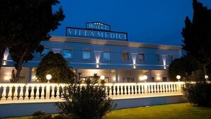 Ein Hotel namens "Hotel Villa Medici" mit einer klassizistischen Fassade, beleuchteten Fenstern und einem gepflegten Garten.