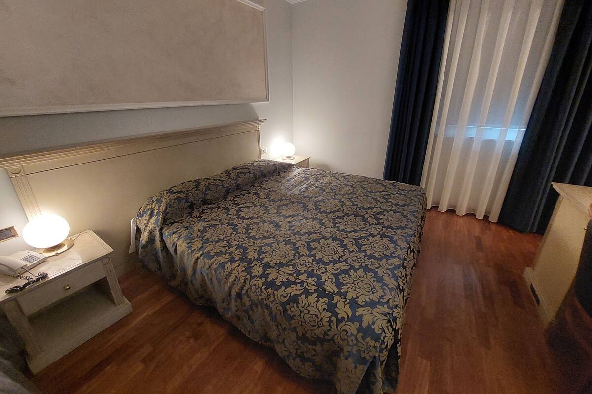 A hotel room with a large bed, a bedside table with a lamp, and a window with curtains.