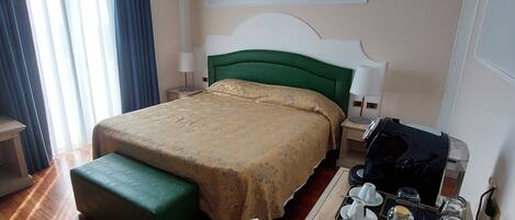 Habitació d'hotel amb un llit, una taula de treball amb una cafetera, un bullidor d'aigua i un comandament a distància.