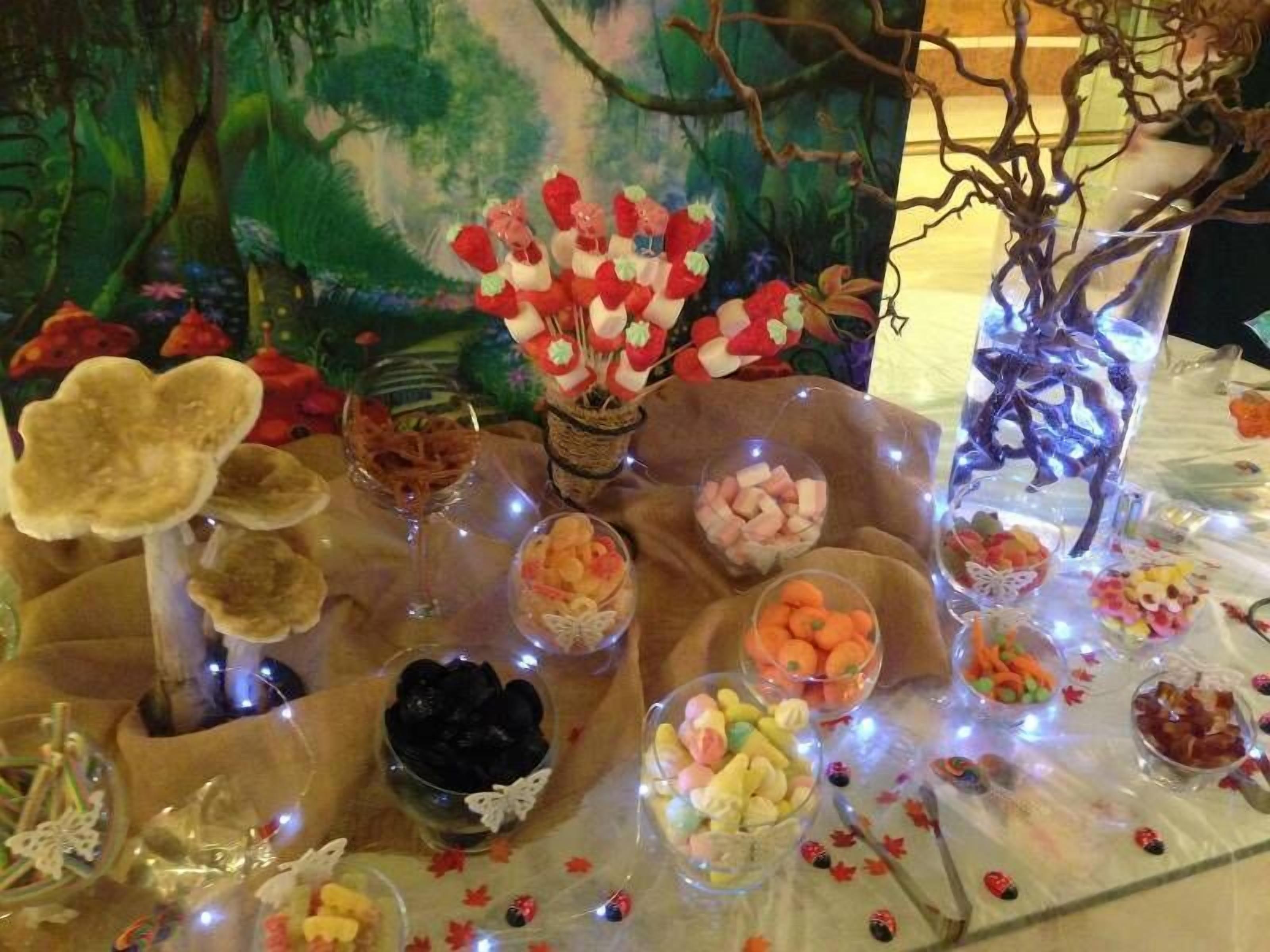 A table with various food items and decorations, set against a backdrop of a forest-themed painting.