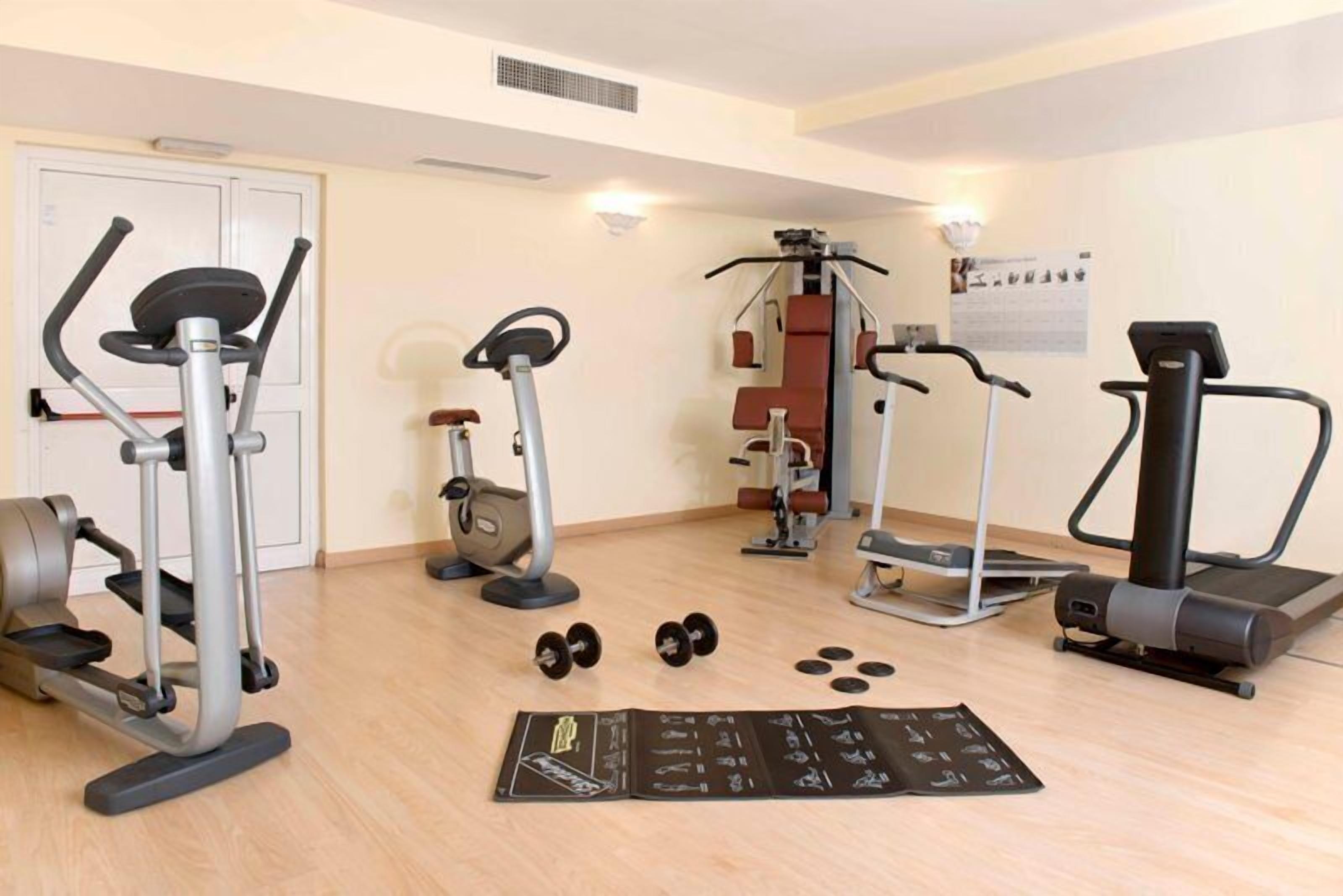 Een fitnessruimte met diverse trainingsapparaten, waaronder loopbanden, elliptische trainers en losse gewichten.