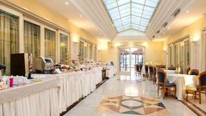 Ein Hotelkorridor mit einer langen Buffettheke, Esstischen und Stühlen, der zu einem Glastür-Eingang führt.