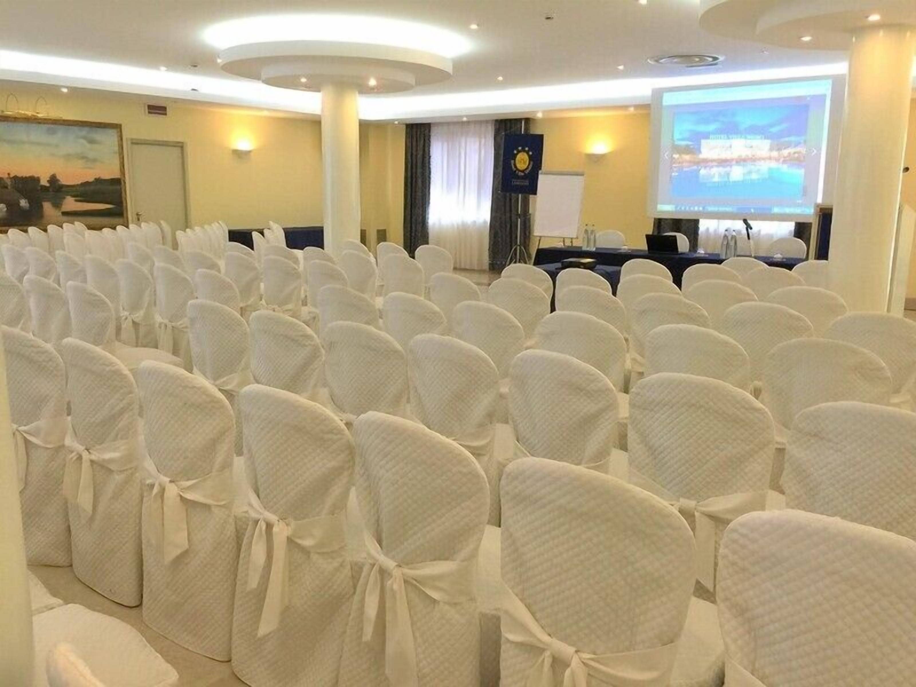 A conference room with rows of white chairs, a projection screen, and a podium.