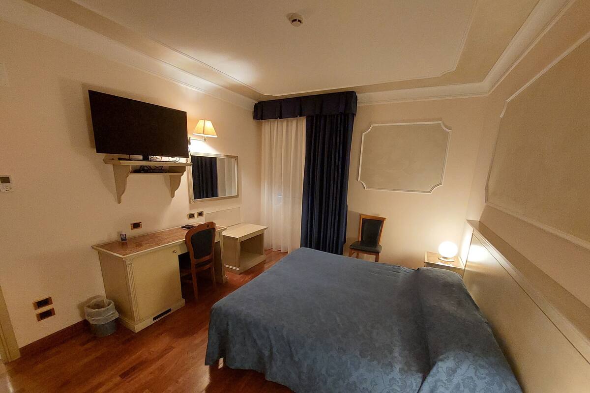 A hotel room with a bed, a desk, a chair, a television, and a window with curtains.