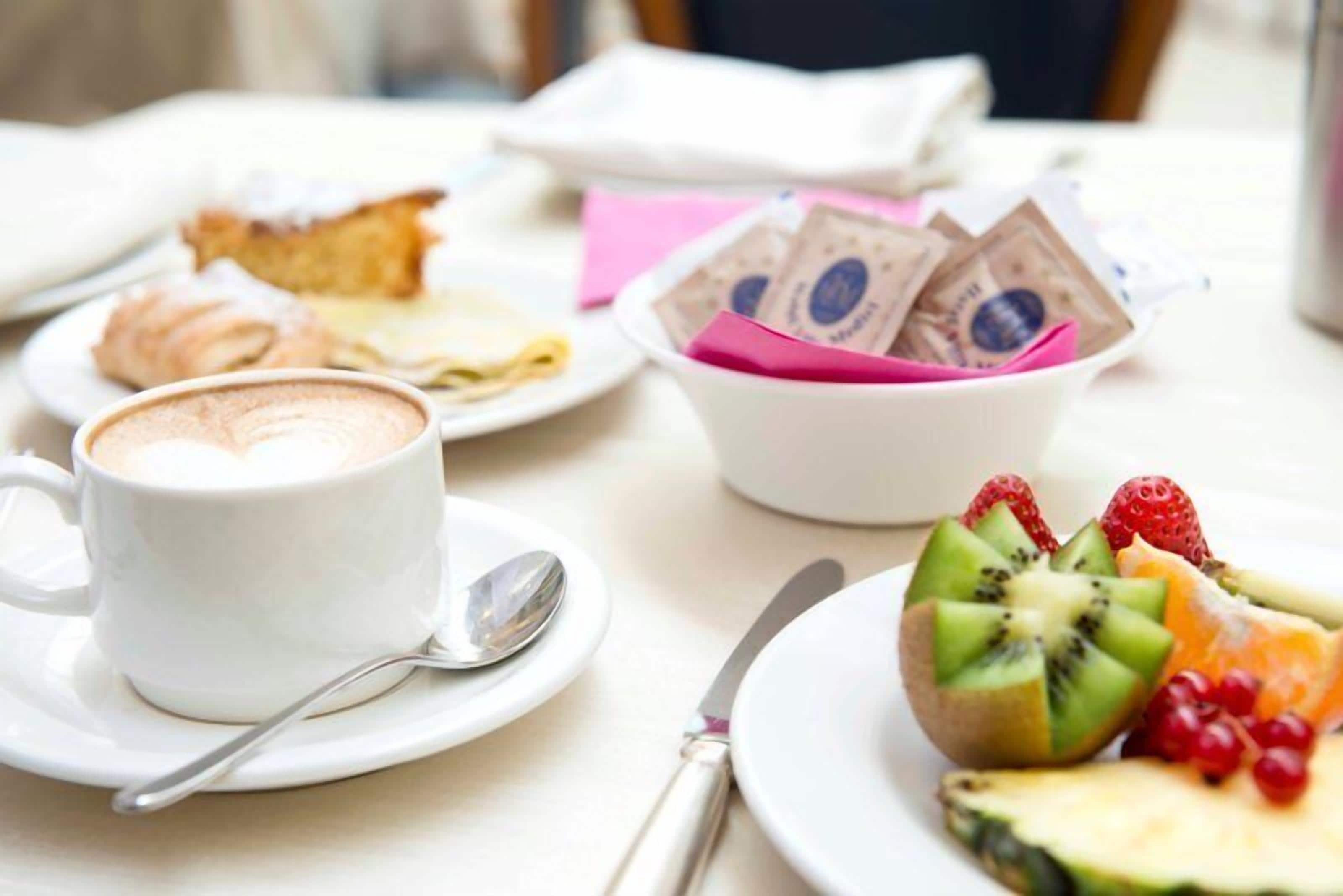 Une table mise pour le petit-déjeuner avec une tasse de café, une assiette de fruits, une pâtisserie et un bol de pièces de chocolat.