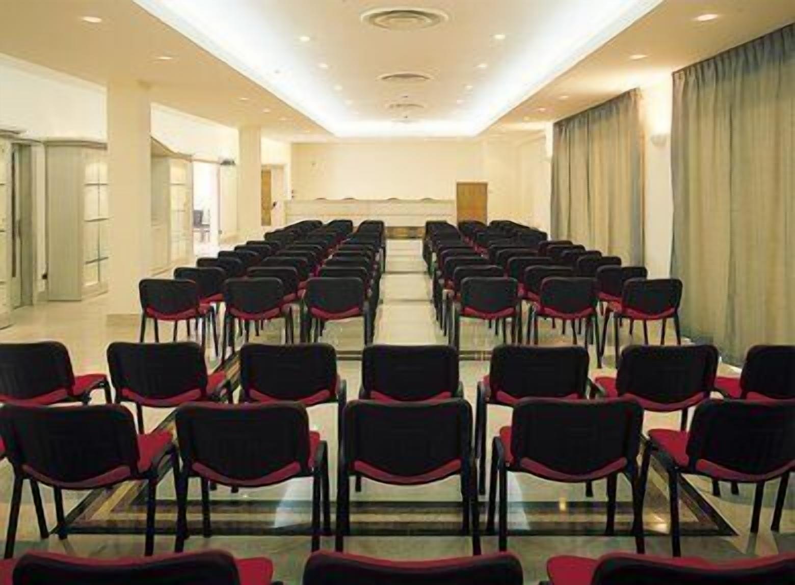 A conference room with rows of black chairs and red cushions, a long table at the front, and a neutral color scheme.