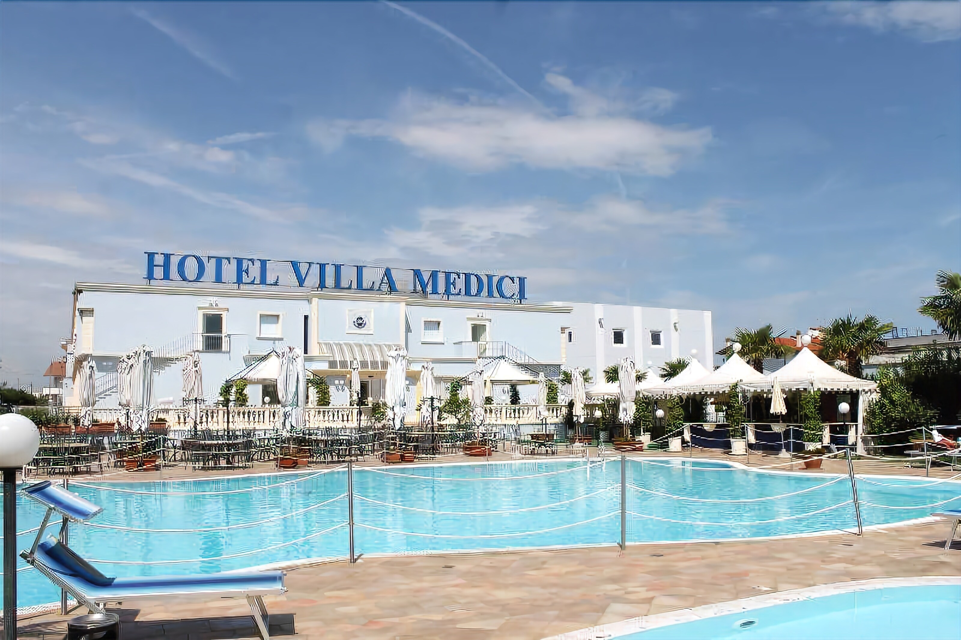 A hotel with a swimming pool, outdoor seating, and a clear sky.