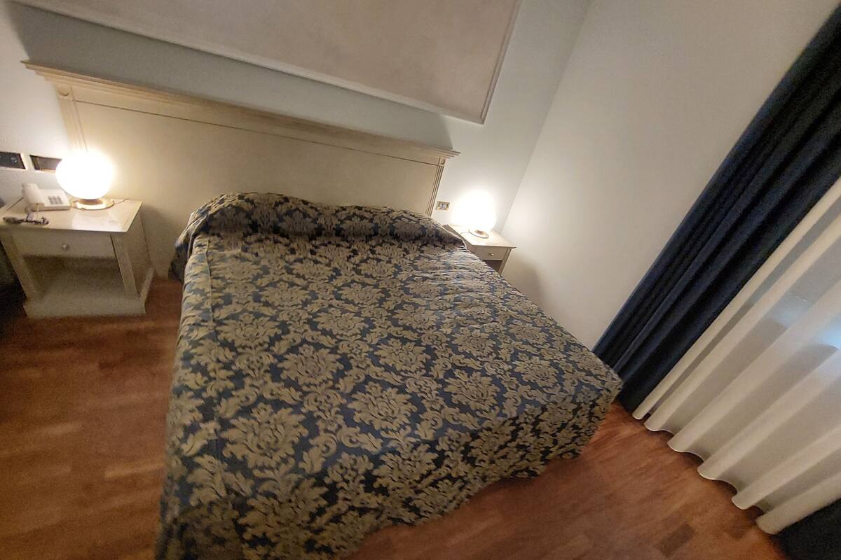 A bedroom with a patterned bedspread, a nightstand with a lamp, and a window with curtains.