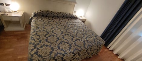 Un dormitorio con una colcha estampada, una mesita de noche con lámpara y una ventana con cortinas.