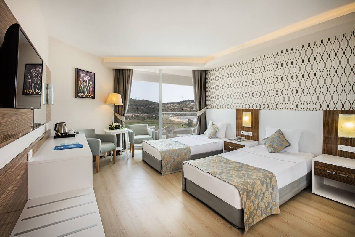 Une chambre d’hôtel avec deux lits, un bureau, une chaise, une télévision et une vue sur le paysage.