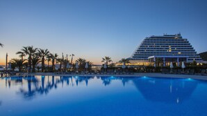 Un grand hôtel doté d’une piscine, de palmiers et de chaises longues.