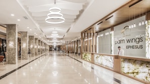 Un hall d’hôtel moderne avec un comptoir d’accueil en marbre, un long couloir doté d’un sol réfléchissant et un plafond orné de luminaires circulaires.