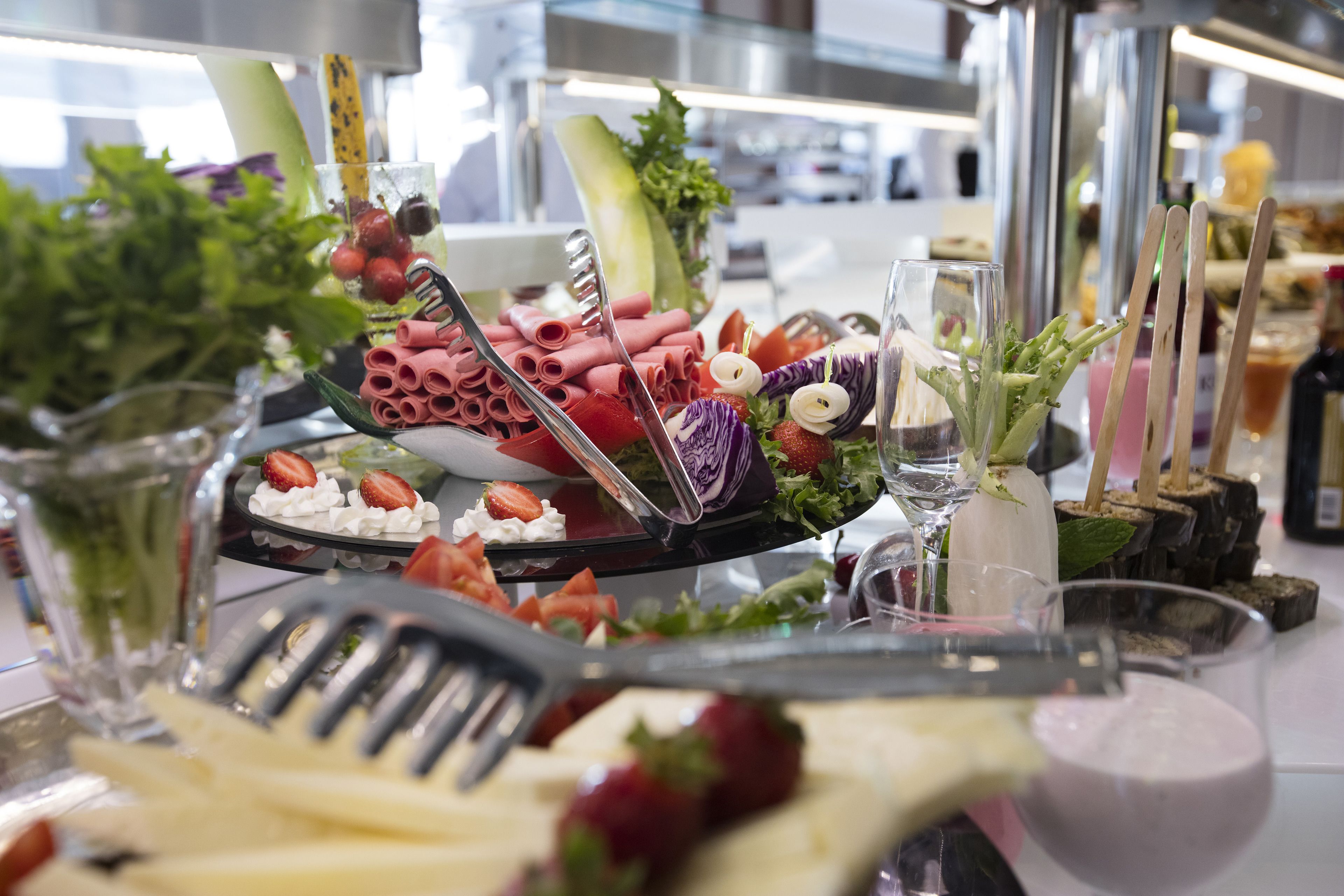A buffet table with various food items, including meats, cheeses, and fruits, arranged on a glass platter.