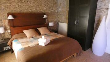 Un dormitorio con cama de madera, paredes de piedra, un armario oscuro y un florero blanco.