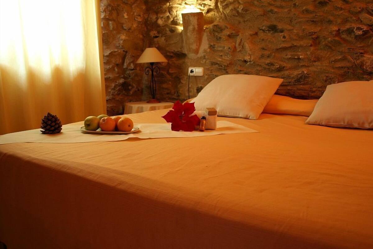A bed with a beige bedspread, a nightstand with a lamp, and a fruit plate with pineapple, apples, and oranges.
