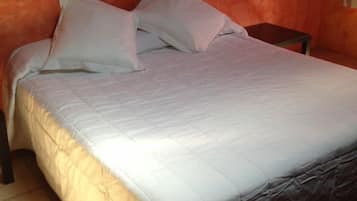 Un lit recouvert d’une courtepointe blanche et agrémenté d’oreillers, une table de chevet et un mur dont le revêtement présente une texture orange.