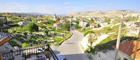 A view from a balcony overlooking a town with a winding road, buildings, and a mountainous backdrop.