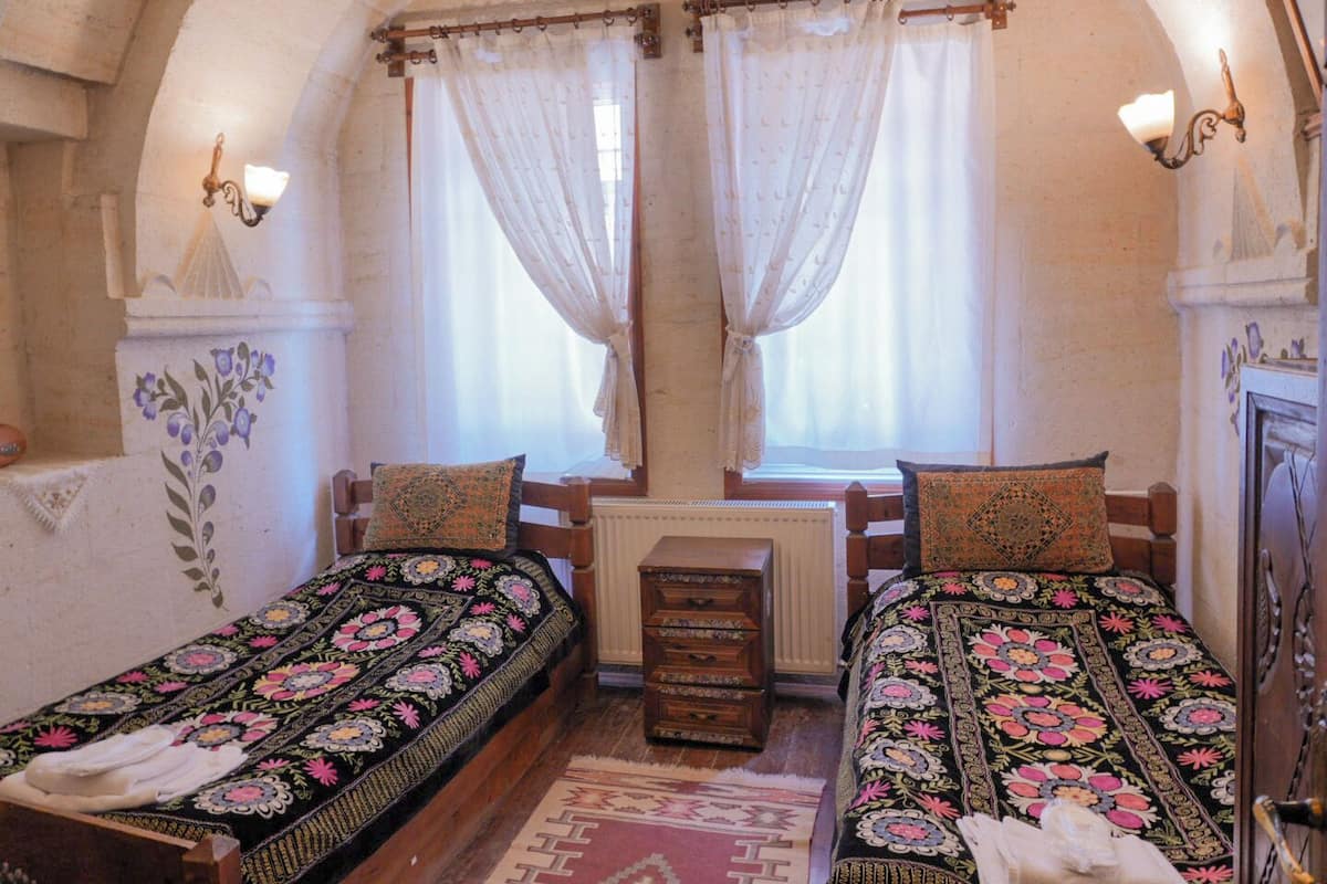 Ein Zimmer mit zwei Holzbetten, jedes mit einer blumigen Tagesdecke, einer kleinen Holzkiste und einem Heizkörper dazwischen.