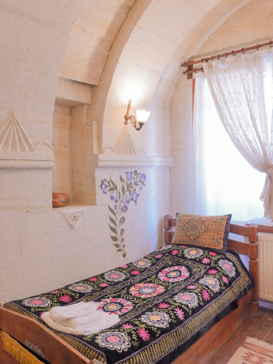 A bedroom with a wooden bed, a decorative wall, a light fixture, and a window with curtains.