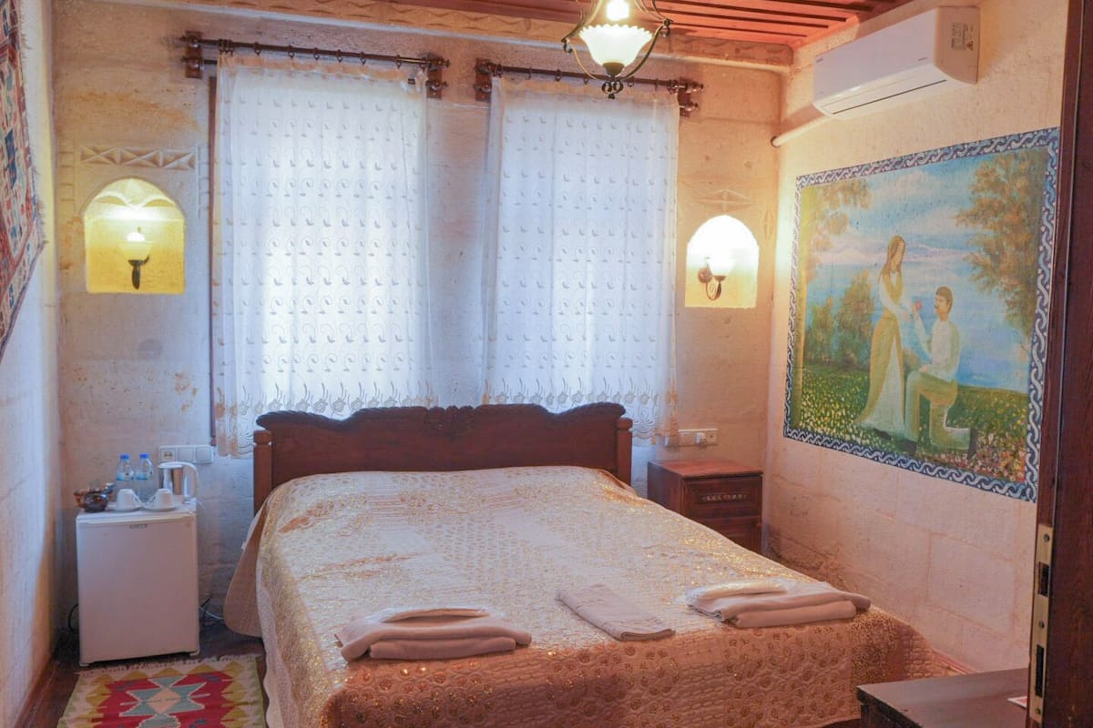 Ein Schlafzimmer mit einem Bett, einem Nachttisch, einer Lampe, einem Gemälde und einem Teppich mit Muster.