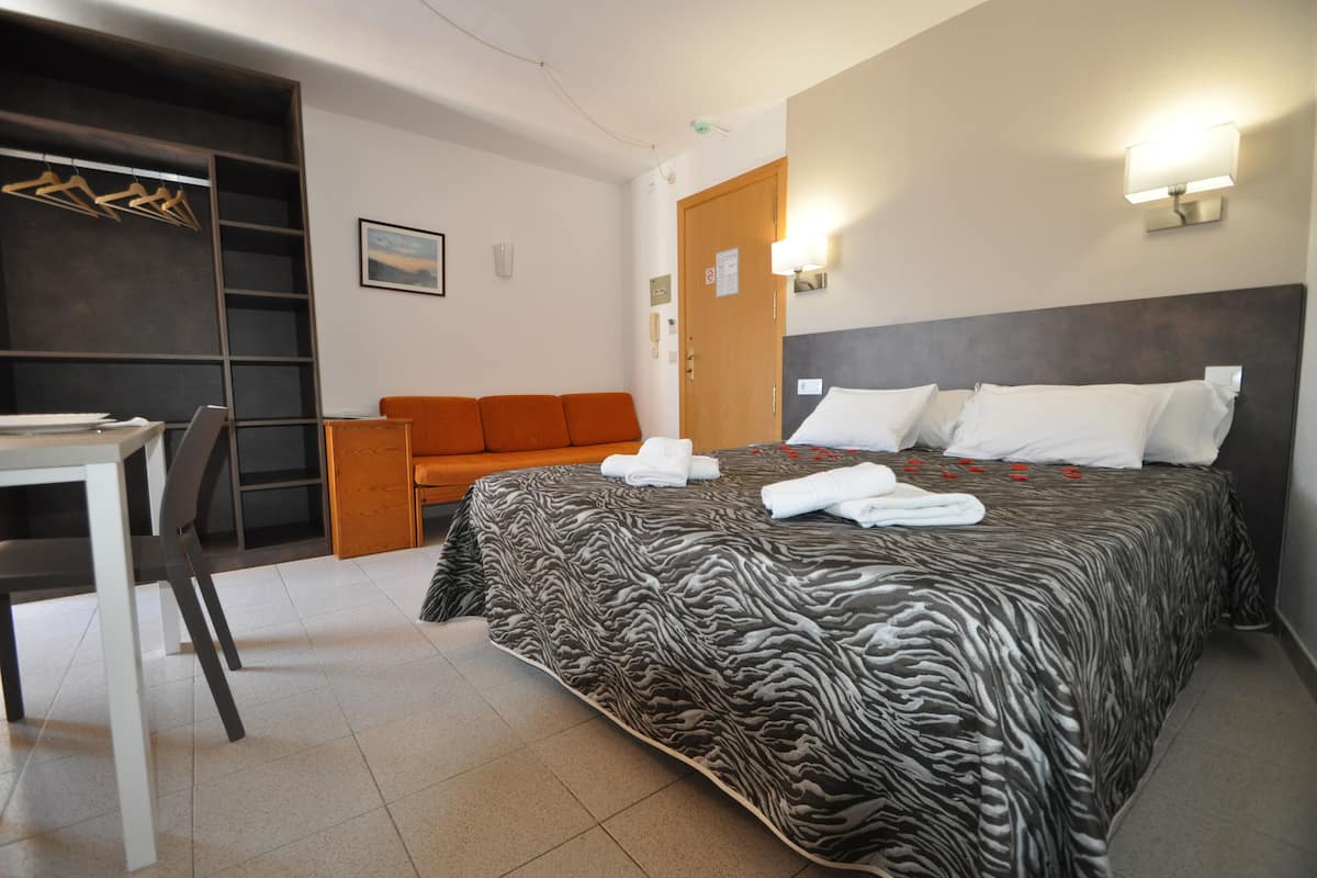 A hotel room with a zebra-patterned bed, a desk, a chair, an orange sofa, and a wardrobe with a ladder.